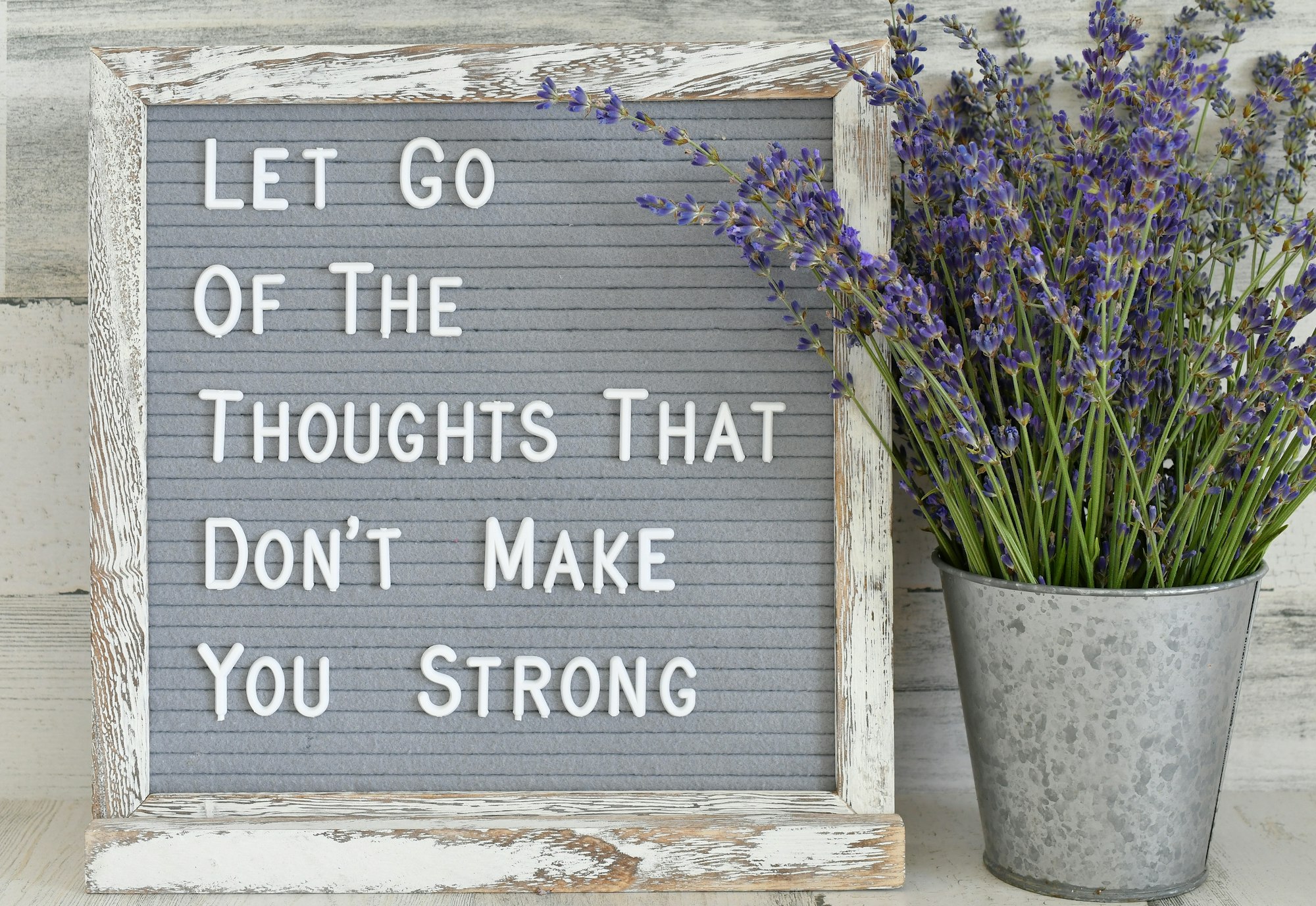 "Let go of the thoughts that don't make you strong" on a gray message board next to lavender bouquet